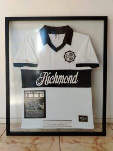 Camiseta histórica del Club Olimpia de 1990 enmarcada en vitrina con moldura negra por Sol y Sombra SRL.