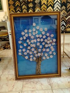 Pintura de árbol con flores en relieve sobre fondo azul, enmarcada con moldura dorada ornamental por Sol y Sombra SRL.