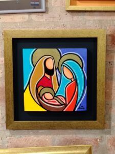 Pintura moderna de la Sagrada Familia en estilo geométrico, enmarcada con moldura dorada y fondo negro por Sol y Sombra SRL.