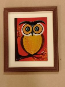 Pintura de un búho colorido con fondo rojo, enmarcada con moldura de madera oscura por Sol y Sombra SRL.