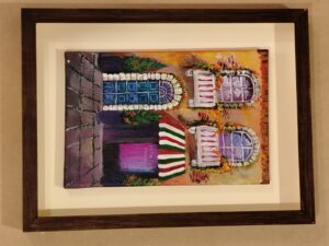 Pintura de fachada colorida con puerta azul y ventanas decoradas, enmarcada con moldura oscura por Sol y Sombra SRL.