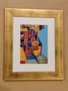 Pintura urbana de casas coloridas con estilo moderno, enmarcada con moldura dorada y passepartout blanco por Sol y Sombra SRL.